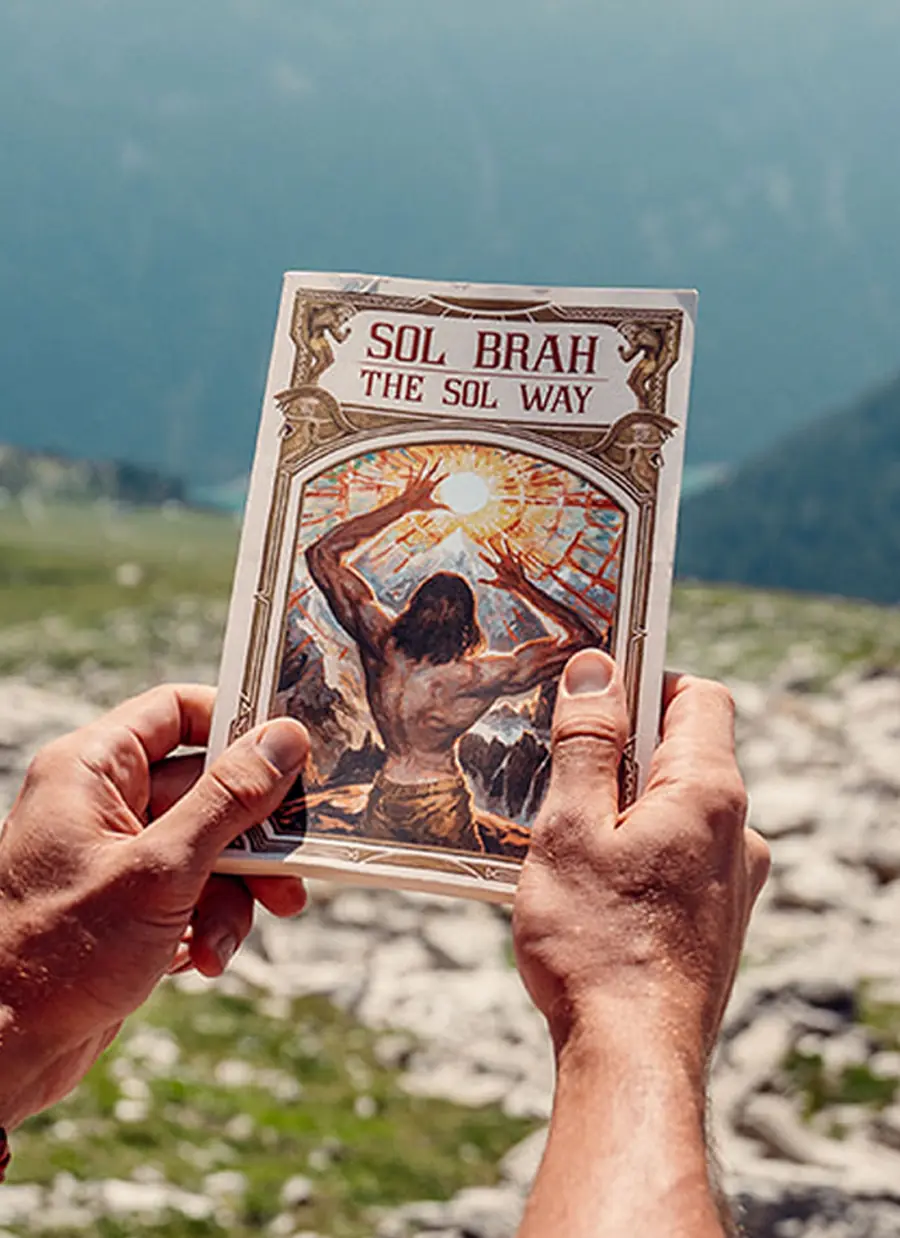 Hands holding The Sol Way by Sol Brah against the mountains