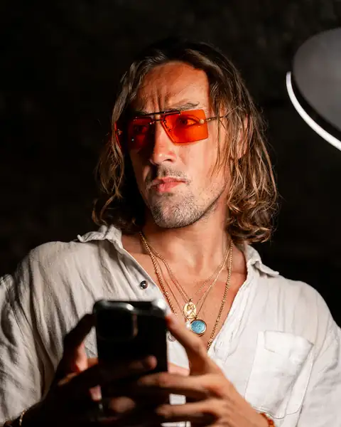Sol Brah in Ra Optics red lenses, checking his phone in a dark room