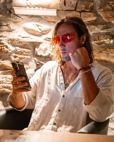 Sol Brah in Ra Optics red lenses, seated by a stone wall